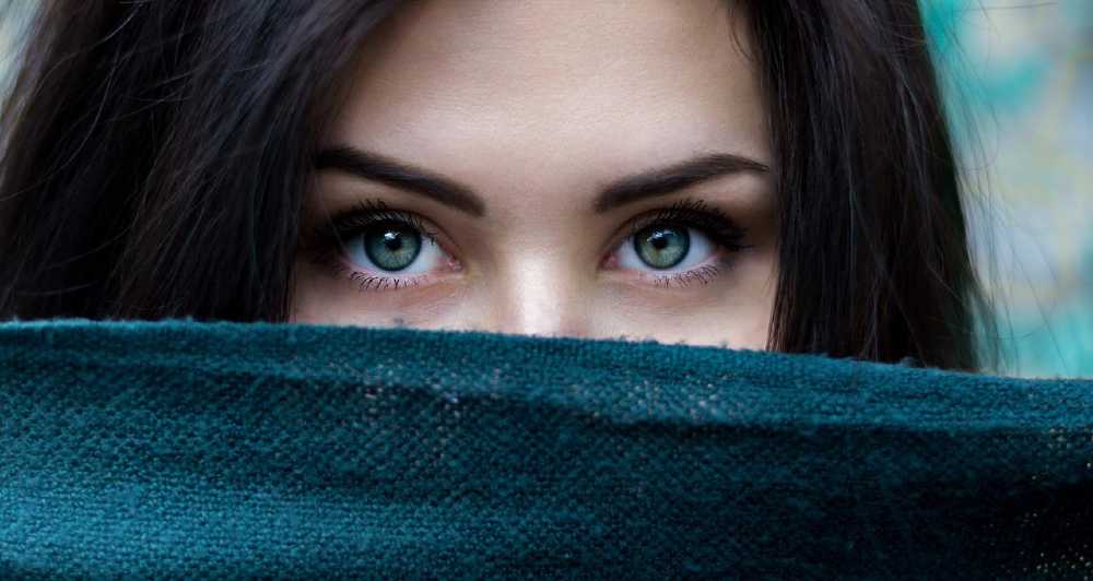 dark haired green eyed woman peeking over cloth