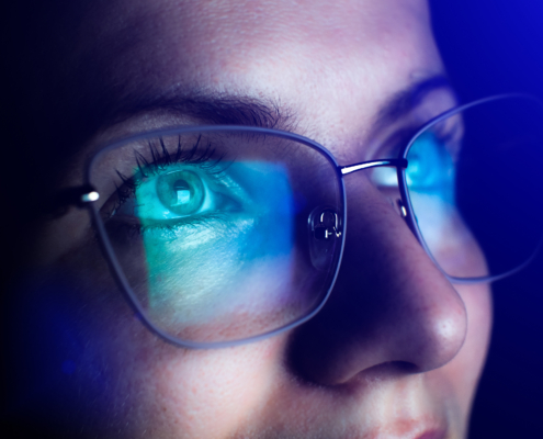 Close-up of a person wearing eyeglasses with blue light reflecting off the lenses