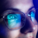 Close-up of a person wearing eyeglasses with blue light reflecting off the lenses